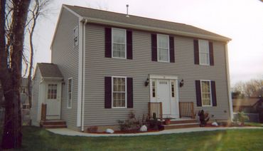 Two-story beige house with white door and black window shutters.