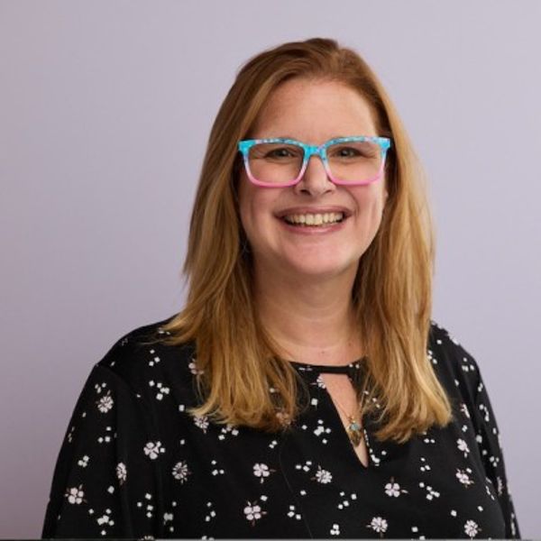 Smiling woman with colorful glasses and floral black top.