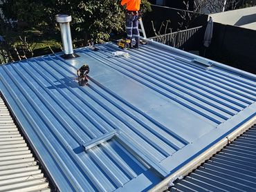 Person working on a blue metal roof on a sunny day.