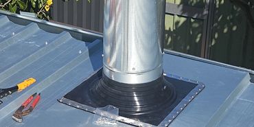 Newly installed metal roof pipe with silicone sealant and tools.