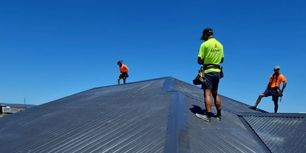 Three workers on a rooftop wearing safety gear under a clear blue sky.