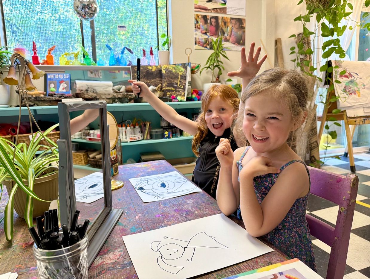 Two girls happily drawing at a colorful art table.