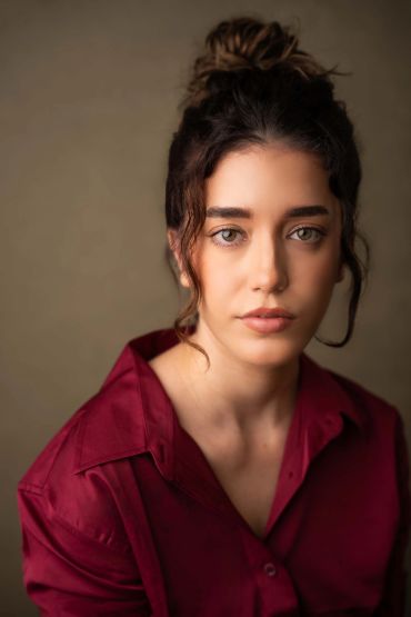 Portrait of a woman in a red shirt with a neutral expression.