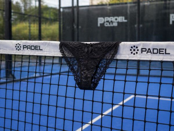 Black lace panties hanging on a Padel tennis net on a blue court.