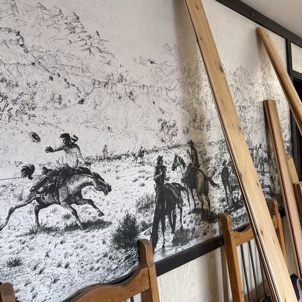 Black and white mural of cowboys on horses in a Western scene.