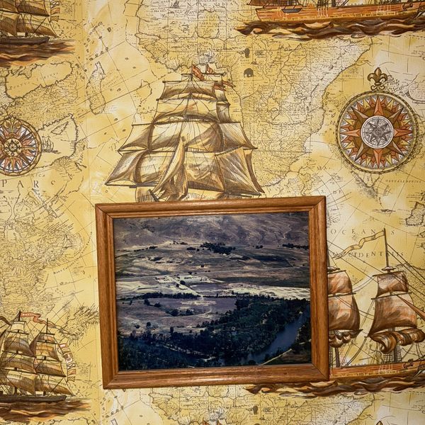 Framed seascape painting on vintage nautical map wallpaper with ships and compass roses.