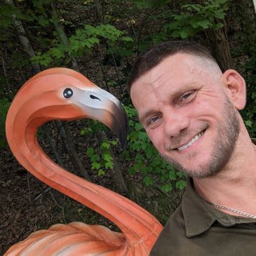 A man smiling next to a large flamingo statue outdoors.