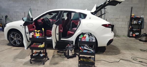 White car with open doors and cleaning supplies in a garage.