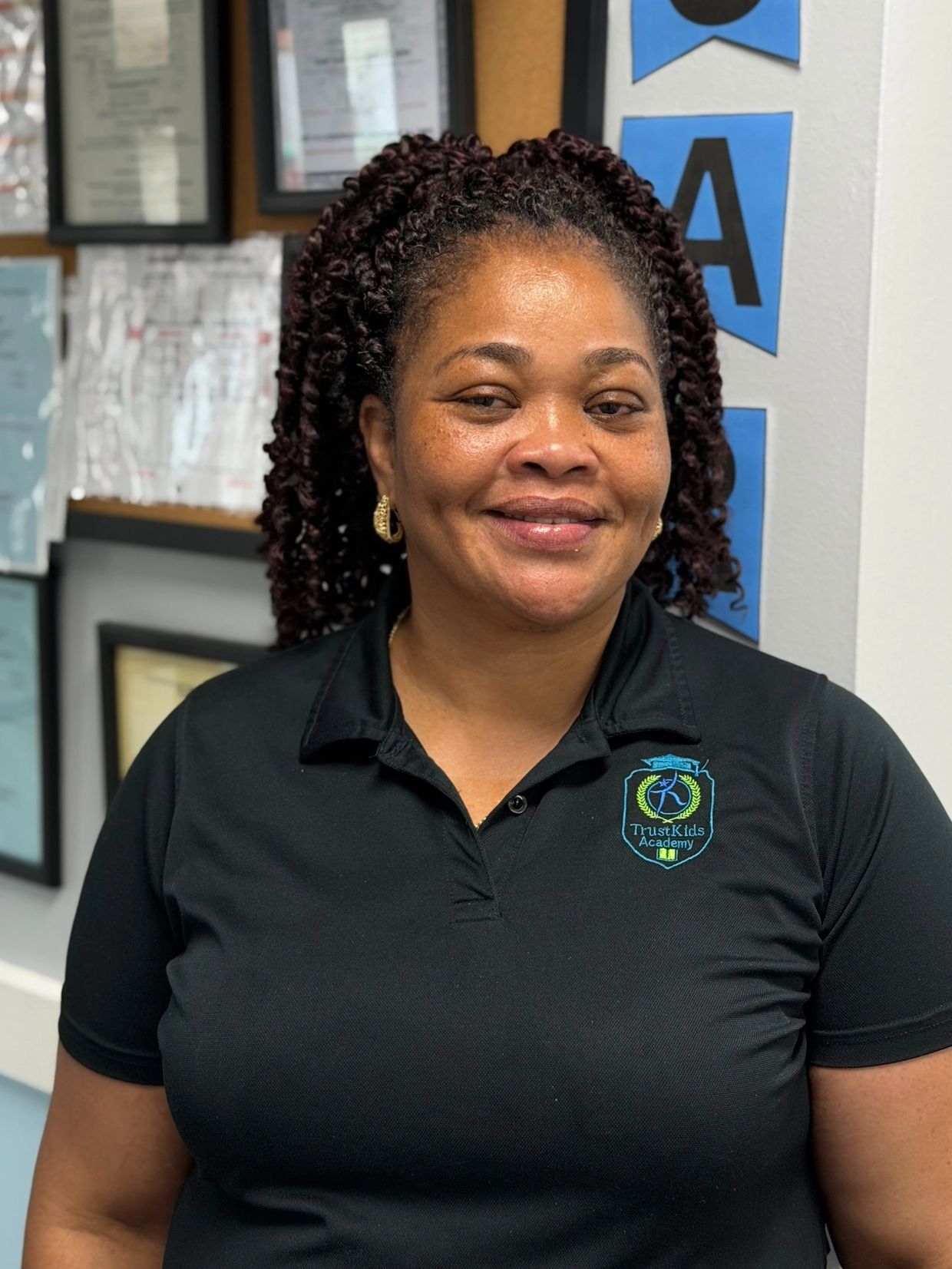 Smiling woman in a black polo shirt with an educational logo.