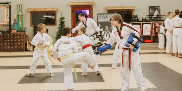 Kids practicing taekwondo with instructor in a dojo.