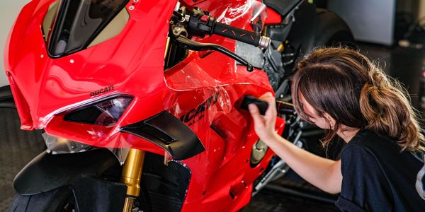Person cleaning a red Ducati motorcycle.