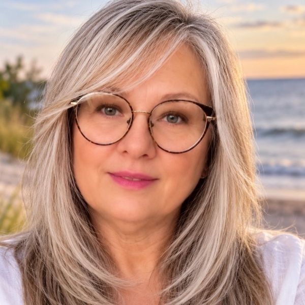 Woman with glasses smiling on a beach at sunset.