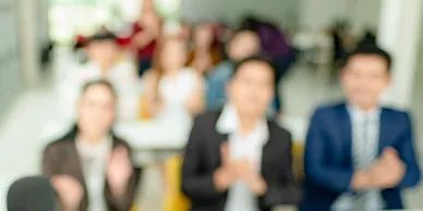 Blurry group of people clapping in a bright indoor setting.