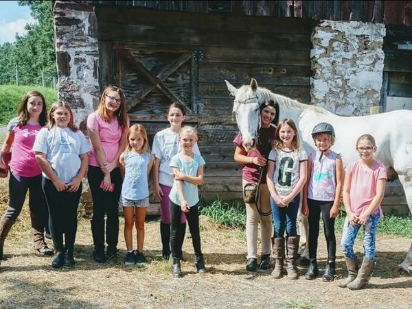 Group of girls posing with a white horse outside a rustic barn.