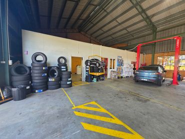 Tire shop with stacked tires and a car on a lift inside a spacious garage.