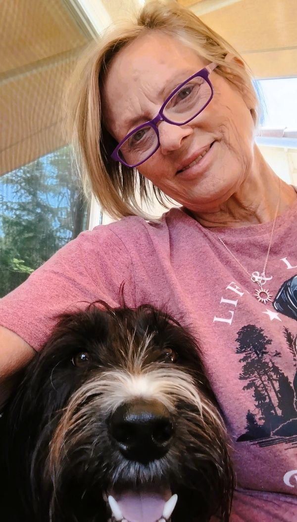 Woman with purple glasses smiling with a black and white dog.