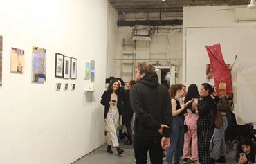 Spectator looking at artwork and group of people behind conversing.