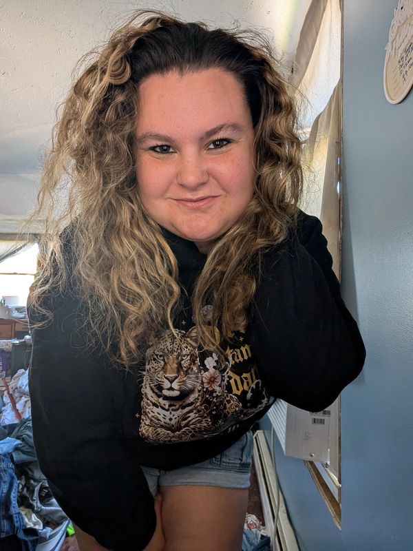 Woman with curly hair wearing a black sweatshirt with a leopard design.