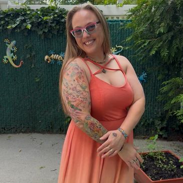 Smiling woman with colorful sleeve tattoo in an orange dress outdoors.
