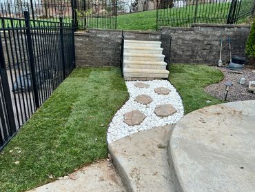 A backyard stone pathway with white pebbles and grass on either side.