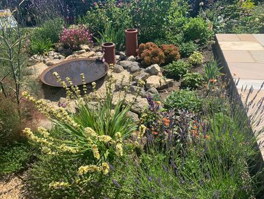 Back garden with a no-lawn scheme, planting and a dried river bed with rockery and corten steel refl