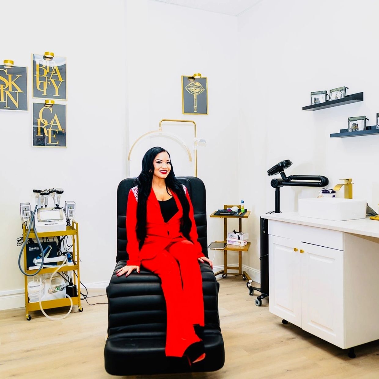 A woman in a red suit sitting on a black chair in a modern beauty clinic.
