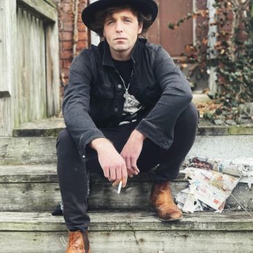 Man in black outfit and brown boots sitting on wooden steps.