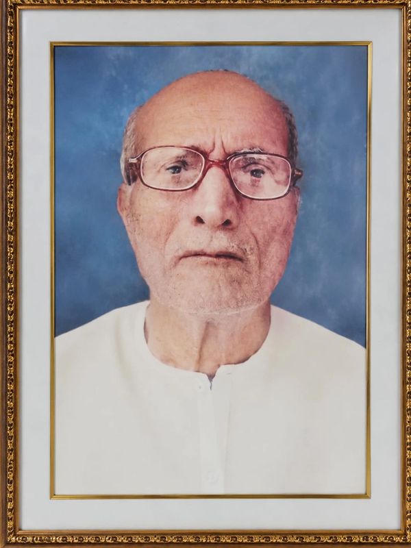 Framed portrait of an elderly man with glasses against a blue background.