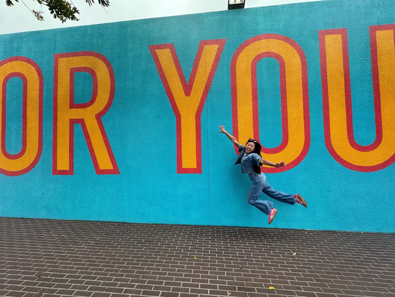 Person joyfully jumping in front of a colorful mural with large letters.