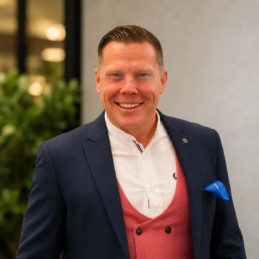 Smiling man in a navy blazer and red vest.