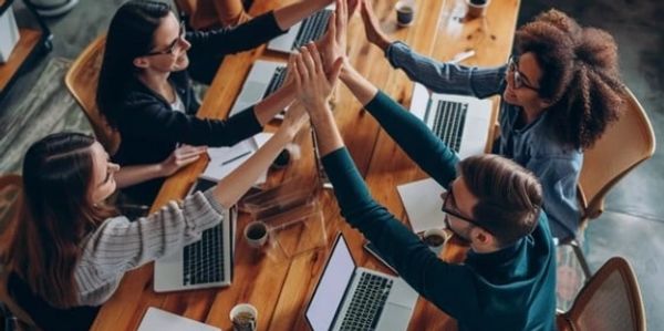 A group of coworkers giving a high-five around a table with laptops.