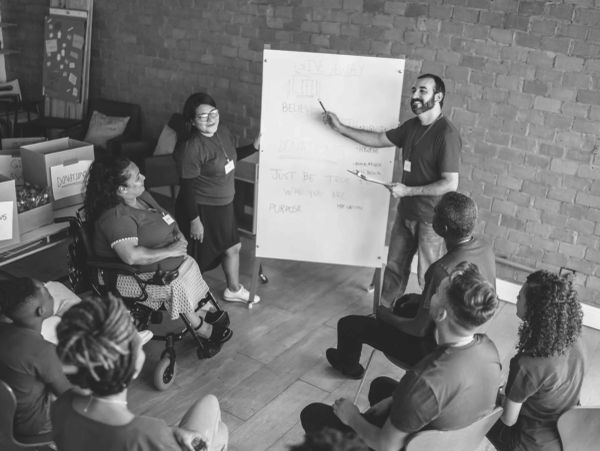 Man presenting ideas on whiteboard to seated group.