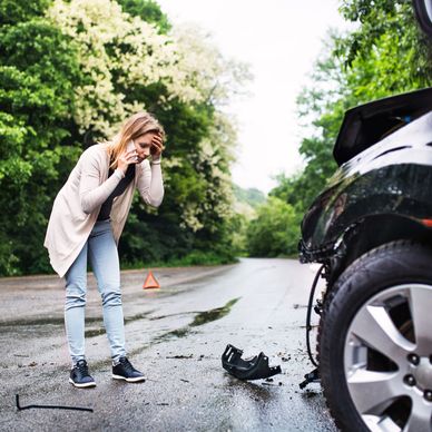 A woman in distress standing in the road talking on the phone after a car wreck