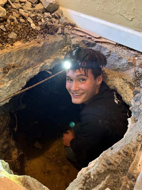 Young man wearing a headlamp sitting inside a hole in the ground indoors.