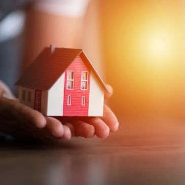 Hand holding a small model house with sunlight in the background.