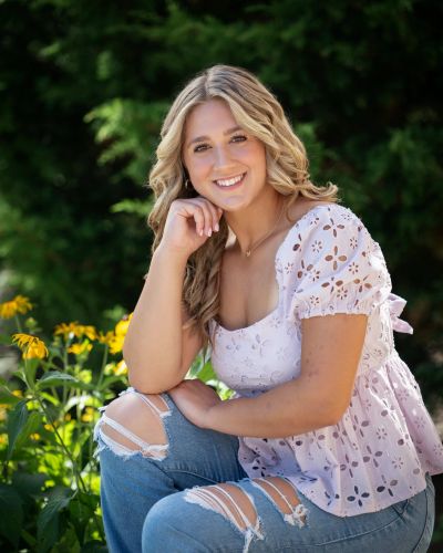 Young woman with blonde hair in a purple blouse and ripped jeans.
