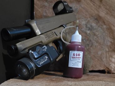 A pistol with a mounted flashlight and a bottle of SSO lubricant on a wooden surface.