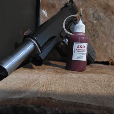 Close-up of a handgun and a bottle of SSO lubricant on a wooden surface.