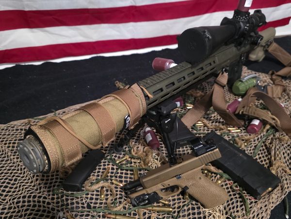 Military-style rifles, pistol, and grenades displayed with American flag backdrop.