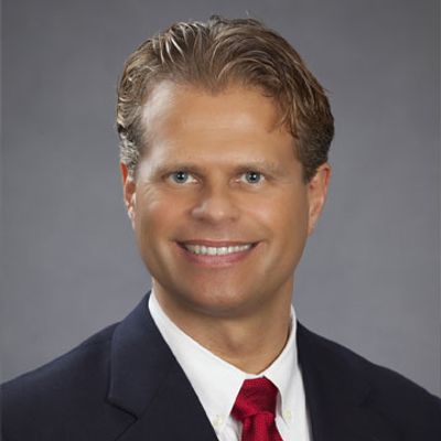 Professional man in suit smiling, gray background.