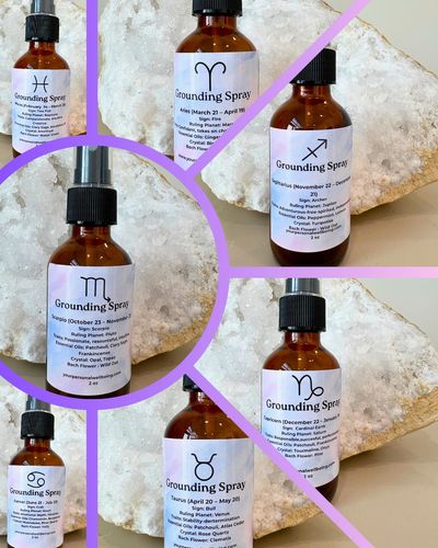 Bottles of zodiac-themed grounding sprays arranged on a rock background.