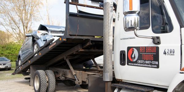 Red Baron Towing flat bed tow truck hauling a car that has been in a collision