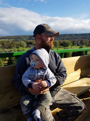 A man with a beard holding a baby on a wooden bench outdoors.