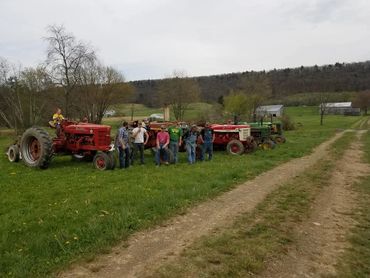 A group of people standing by vintage tractors on a rural farm.