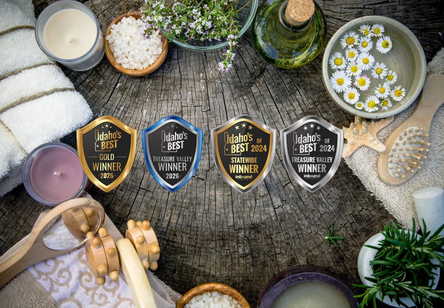 A rustic spa setup with candles, towels, flowers, and award badges on a wooden surface.