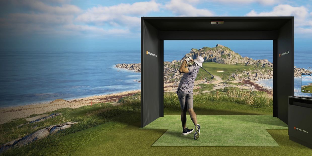 Man hitting golf ball into simulator that expands into a real-world golf course