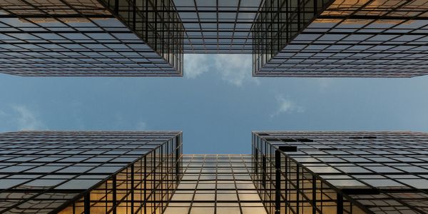 View looking up between two tall glass skyscrapers under a blue sky.