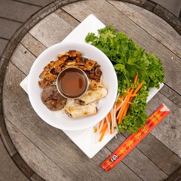 Vietnamese dish with grilled meat, spring rolls, fresh herbs, and dipping sauce.