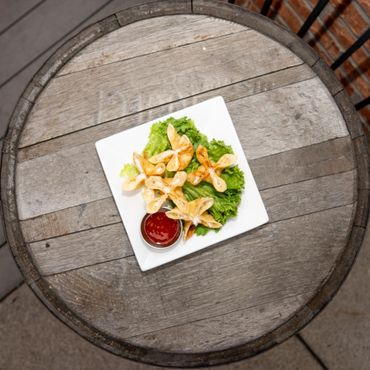 Star-shaped fried wontons on lettuce with dipping sauce on a wooden barrel table.