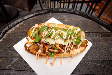 Spicy sandwich with grilled meat, fresh veggies, and creamy sauce on a toasted bun.